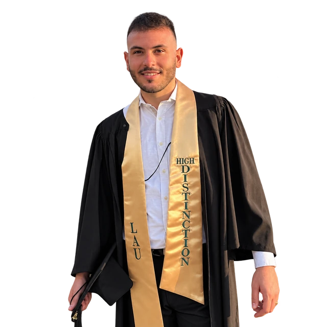 Alex in his LAU graduation gown and gold High Distinction stole, holding his cap.