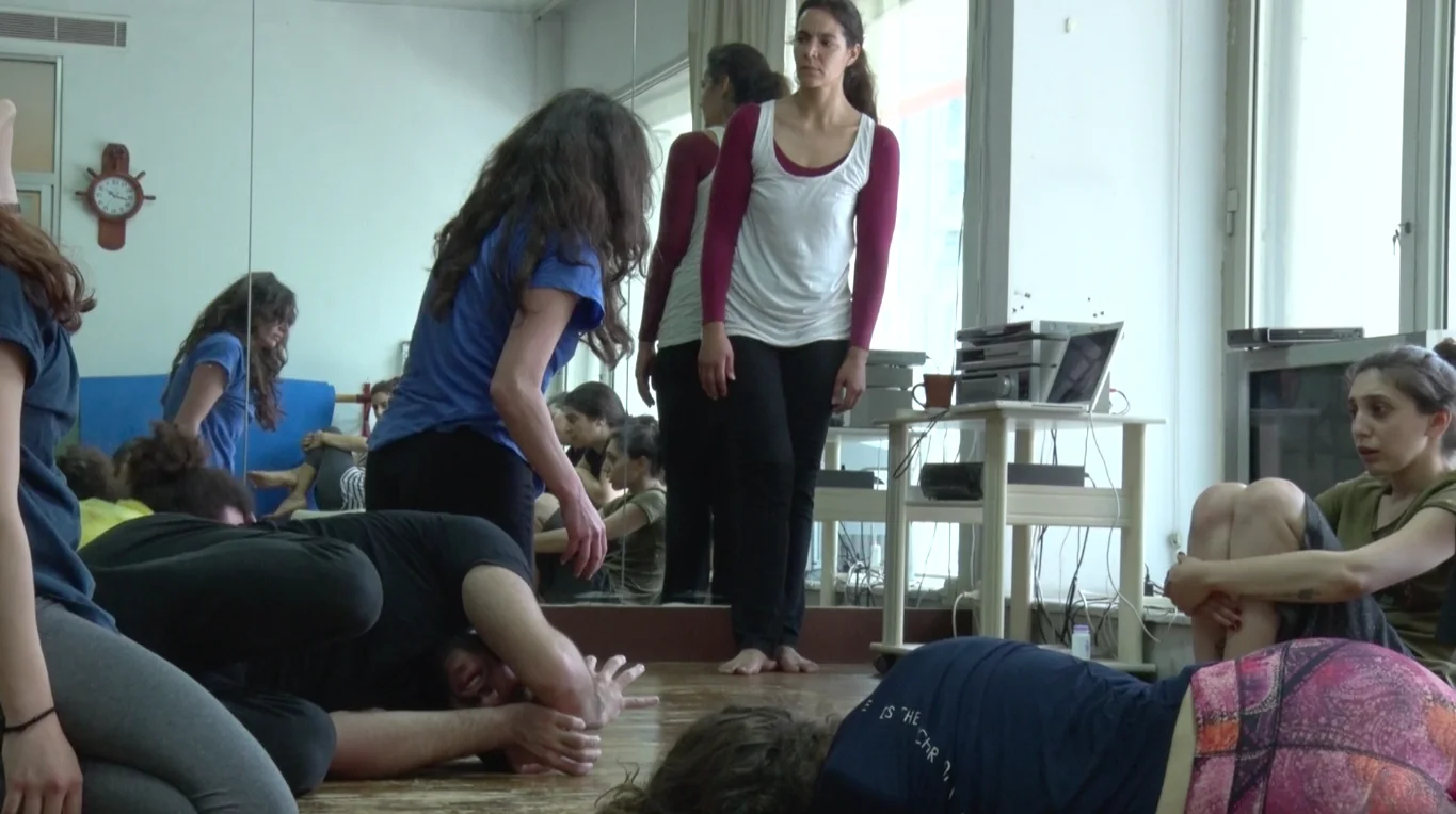 Participants practise movement on a studio floor while the workshop leader observes.