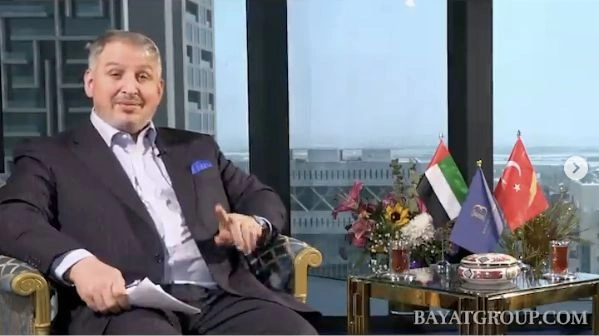 Israfil Kahraman seated in the Bayat interview setting beside Turkish and Emirati flags.