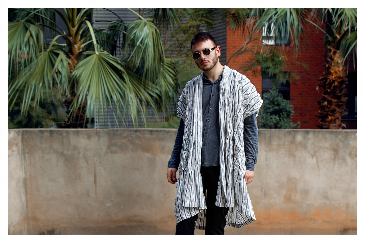 Alex modelling a layered Khair Everywhere garment in a courtyard with palms · Khair Everywhere