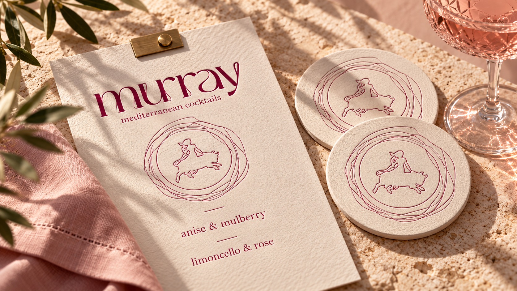 A cream Murray cocktail menu with embossed emblem coasters, blush linen, a brass clip and crystal glassware.