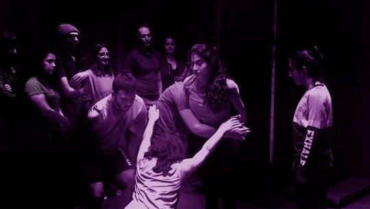 Performers and audience members in Mining the Gap, under violet stage lighting