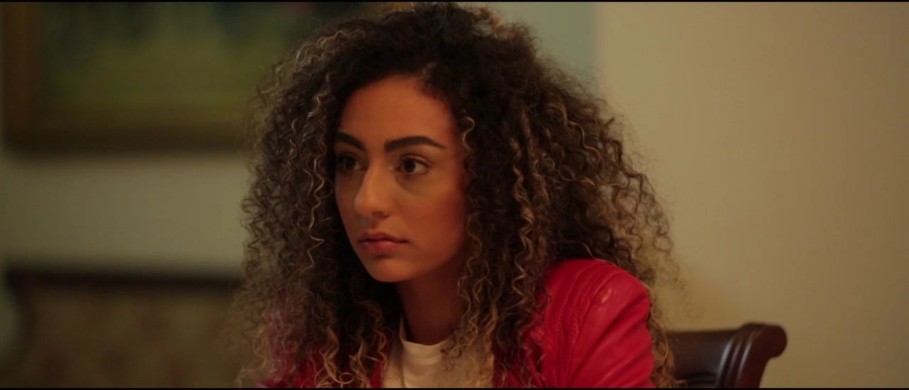 A woman in a red cardigan turns toward someone at the dinner table.