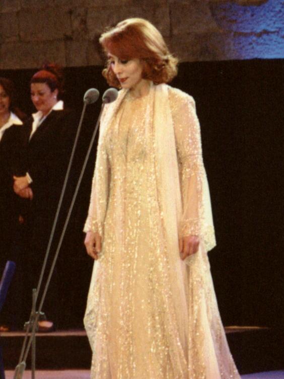 Fairuz singing into a microphone on stage in a gold dress.