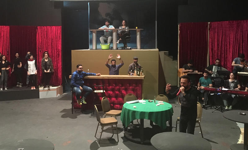 The Casino el-Ons stage with red curtains, singers, musicians, a poker table and a raised news desk.