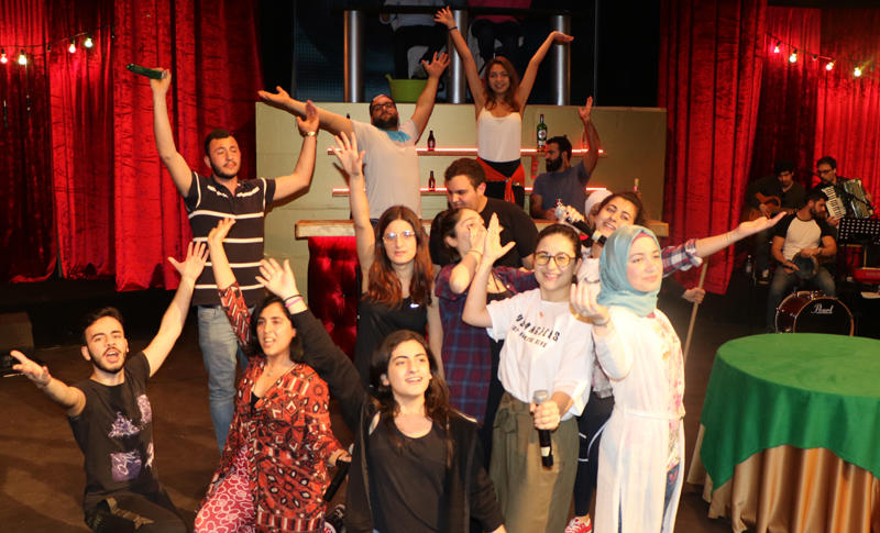 The Casino el-Ons ensemble with raised arms among the cabaret set and musicians.
