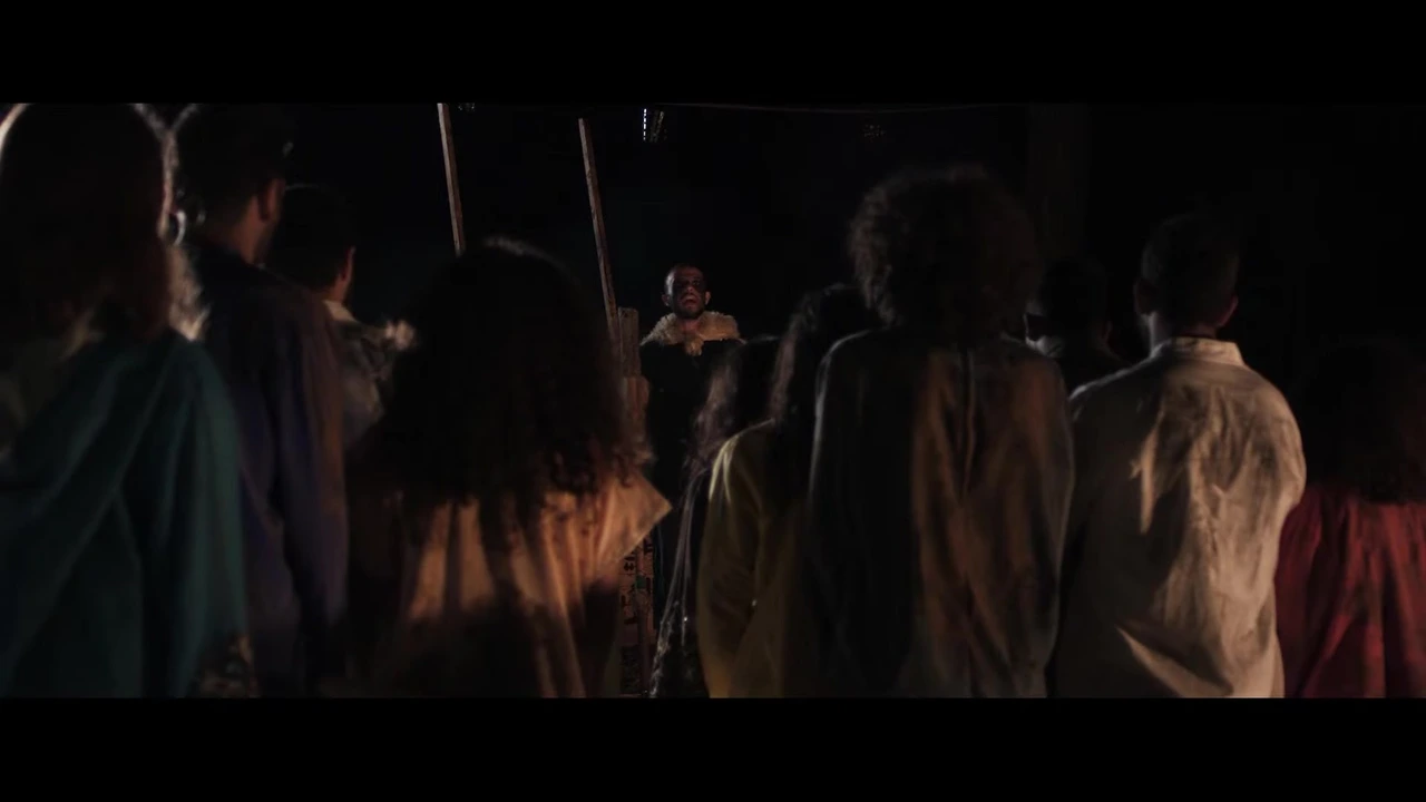 An ensemble gathered around a costumed figure in a firelit scene from The Getaway. · The Getaway